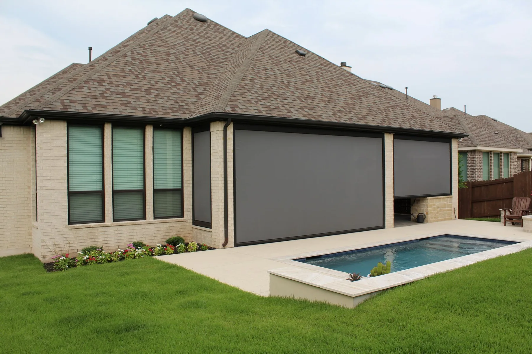 Brick home pool patio with wide motorized outdoor screens for shade and privacy