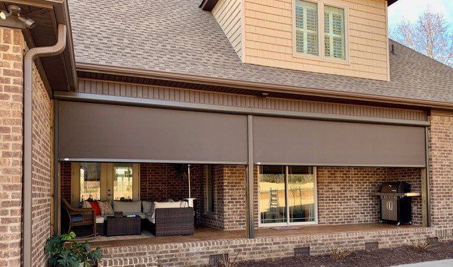 Covered brick patio with two shades lowered across the opening